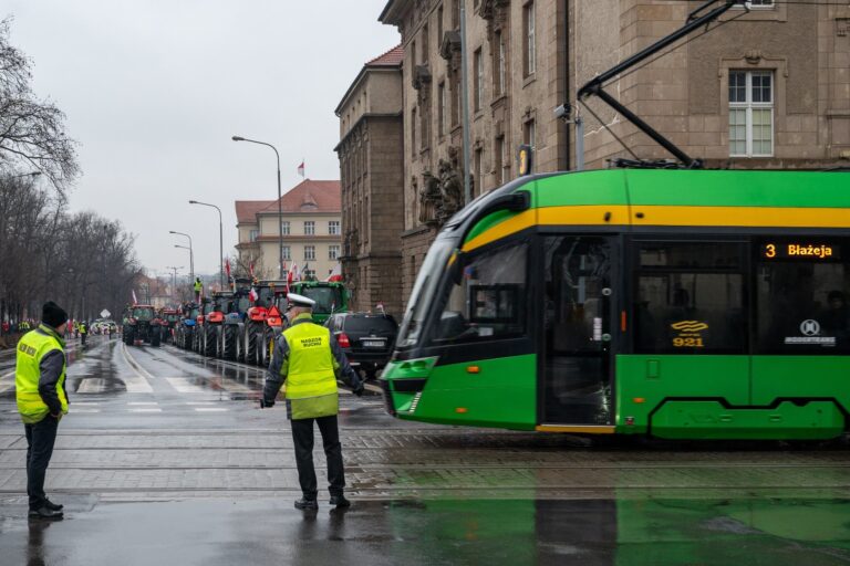 Pracownicy Nadzoru Ruchu MPK Poznań na skrzyżowaniu. Obok tramwaj, w tle mnóstwo traktorów